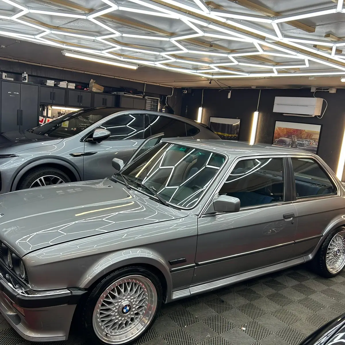 Sølvgrå BMW E30 og en grå elbil parkert i studioet under sekskantriggen